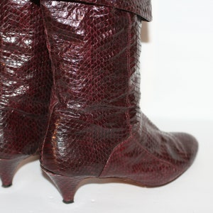 May include: A pair of burgundy leather boots with a snakeskin pattern and a low heel.