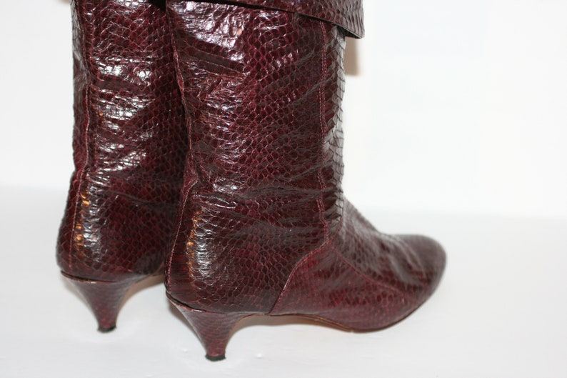 May include: A pair of burgundy leather boots with a snakeskin pattern and a low heel.