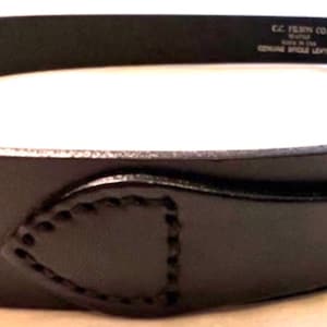 K&ouml;nnte beinhalten: Nahaufnahme eines schwarzen Lederg&uuml;rtels mit einem gen&auml;hten Design in der N&auml;he der Schnalle. Der G&uuml;rtel tr&auml;gt den Text "C.C. FILSON CO. SEATTLE MADE IN USA GENUINE BRIDLE LEATHER".