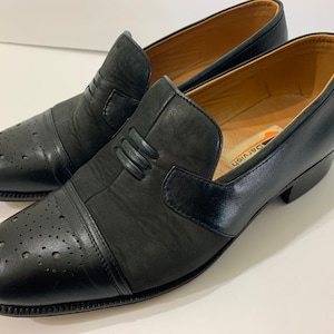 May include: A pair of black leather slip-on shoes with a perforated design on the toe. The shoes have a Dervish label on the inside.