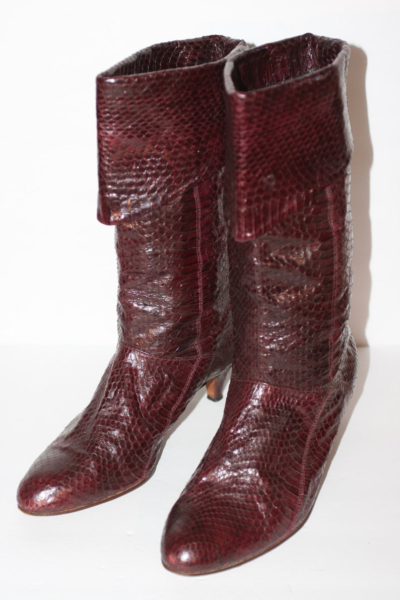 May include: A pair of brown leather boots with a snakeskin pattern. The boots have a low heel and a pointed toe.