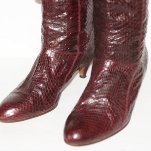May include: A pair of burgundy knee-high boots with a snakeskin pattern and a low heel.
