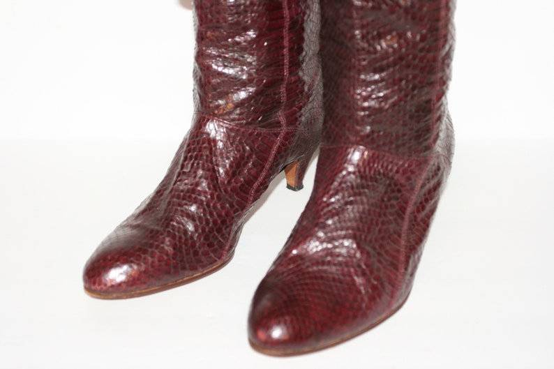 May include: A pair of burgundy knee-high boots with a snakeskin pattern and a low heel.