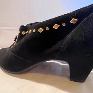 May include: Black suede ankle boots with a gold diamond-shaped embellishment on the top of the shoe.