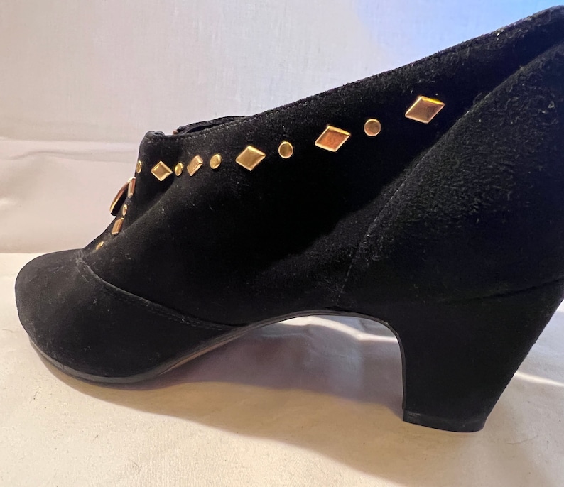 May include: Black suede ankle boots with a gold diamond-shaped embellishment on the top of the shoe.