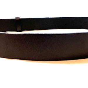 K&ouml;nnte beinhalten: Nahaufnahme eines schwarzen Lederg&uuml;rtels. Der G&uuml;rtel hat ein schlichtes Design mit einer rechteckigen Schnalle und einer einzelnen G&uuml;rtelschlaufe. Das Leder scheint glatt und leicht gl&auml;nzend zu sein.