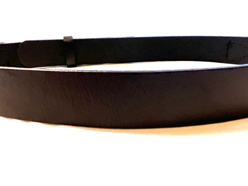 K&ouml;nnte beinhalten: Nahaufnahme eines schwarzen Lederg&uuml;rtels. Der G&uuml;rtel hat ein schlichtes Design mit einer rechteckigen Schnalle und einer einzelnen G&uuml;rtelschlaufe. Das Leder scheint glatt und leicht gl&auml;nzend zu sein.