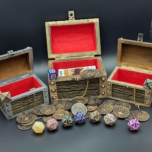 Könnte beinhalten: Drei offene Schatzkisten mit roten Samtinnenräumen, umgeben von Goldmünzen und bunten polyedrischen Würfeln. Die Truhen sind aus Holz mit Metallakzenten. Ein lustiges Set für Tabletop-Spiele.
