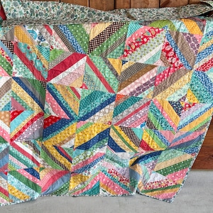May include: A patchwork quilt featuring a vibrant array of multi-colored fabric strips arranged in a geometric star pattern. The textile displays a diverse collection of floral, polka dot, and striped prints in shades of red, blue, yellow, and green.