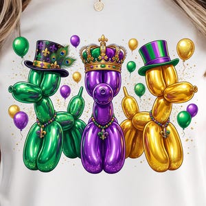 Könnte beinhalten: Ein weißes T-Shirt mit einer lebendigen Illustration von drei Ballon-Tieren in Mardi-Gras-Farben. Die grünen, lila und goldenen Ballonhunde tragen Zylinder und Kronen, umgeben von Luftballons und Konfetti. Das Design ist festlich und auffällig.