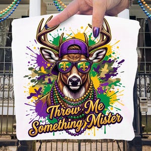 May include: White tote bag with a deer wearing a purple cap and sunglasses with a fleur-de-lis design. The deer has a beaded necklace and the text "Throw Me Something Mister" in gold and purple.