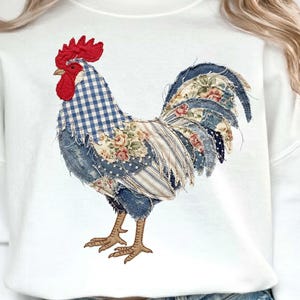 Może przedstawiać: Biała bluza z nadrukiem koguta w stylu patchwork. Kogut ma czerwony grzebień, niebiesko-białą kratkę na szyi i tułów wykonany z kwiatowych i wzorzystych tkanin. Ogon koguta to mieszanka niebieskich kwiatowych i paskowych wzorów.