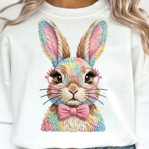Puede incluir: Sudadera blanca con un diseño de conejo colorido. El conejo lleva gafas rosas y una pajarita rosa. El pelaje del conejo es una mezcla de colores pastel, incluyendo rosa, azul, amarillo y marrón.