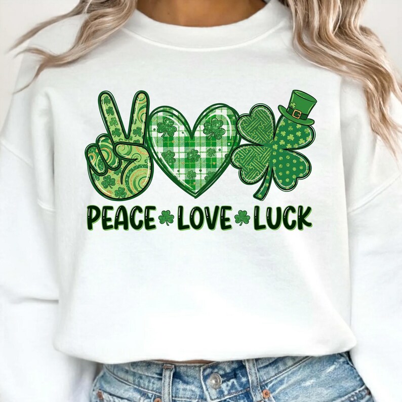 May include: White sweatshirt with a green graphic design featuring a peace sign, heart, and shamrock. The words "PEACE LOVE LUCK" are printed in green below the symbols. The design incorporates various green patterns and a small green hat.