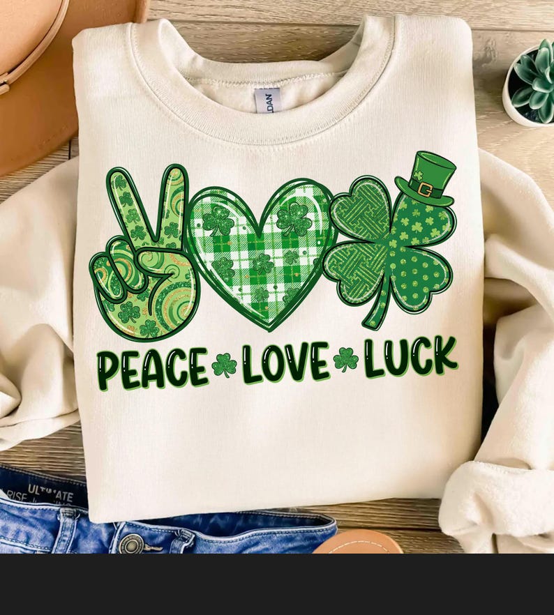 May include: Cream-colored sweatshirt with a St. Patrick's Day graphic. The design includes a peace sign, a heart, and a shamrock, all in shades of green. The words "PEACE LOVE LUCK" are printed below the symbols.