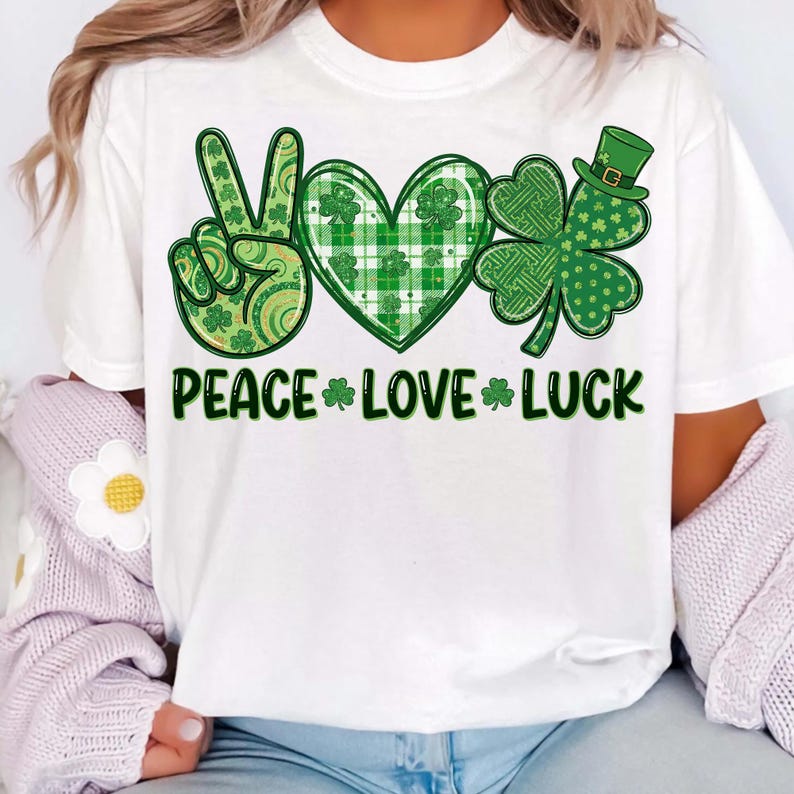 May include: White t-shirt featuring a green and white design with the words "PEACE LOVE LUCK". The design includes a peace sign, a heart, and a four-leaf clover, all in shades of green.