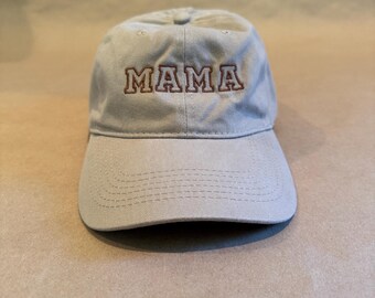May include: A beige baseball cap with the embroidered word "MAMA" in brown letters. The cap has a curved brim and a fabric strap closure. The hat is made of a soft, durable material.