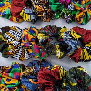 Könnte beinhalten: Eine Sammlung bunter Stoff-Haargummis. Die Haargummis weisen lebendige Muster in Rot, Gelb, Blau, Grün und Orange auf. Die Muster umfassen geometrische Formen und florale Designs. Diese Haaraccessoires sind perfekt, um jeder Frisur einen Farbtupfer zu verleihen.