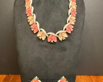 May include: A vintage jewelry set featuring a necklace and matching earrings. The necklace and earrings showcase a floral design with orange and peach-colored petals. The metal components are silver-toned, and the set is displayed on a black mannequin.