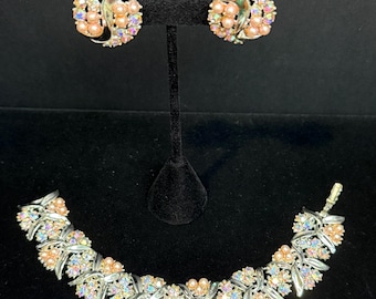 Peut inclure: Un ensemble de bijoux vintage comprenant un bracelet et des boucles d'oreilles assorties. L'ensemble comprend un bracelet argenté avec un motif floral, orné de strass irisés et de fausses perles couleur pêche. Les boucles d'oreilles ont un design similaire.