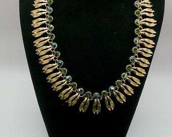 Peut inclure: Un collier doré et un ensemble de boucles d'oreilles assorties. Le collier présente une série de pendentifs dorés en forme de feuilles avec des accents de cristaux verts et bleus. Les boucles d'oreilles sont rondes, avec un design floral et des cristaux verts et bleus assortis.