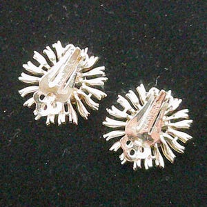 May include: A pair of silver-toned clip-on earrings. Each earring features a sunburst design with radiating lines. The clip mechanism is visible, with the word "EISNER" stamped on the clip.