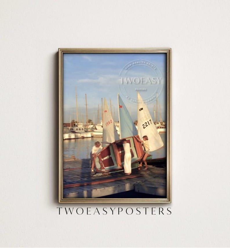 May include: A framed vertical poster featuring a vintage photograph of three individuals on a wooden dock preparing a small sailboat. In the background, several sailboats with white and blue sails are moored in a harbor under a clear sky.