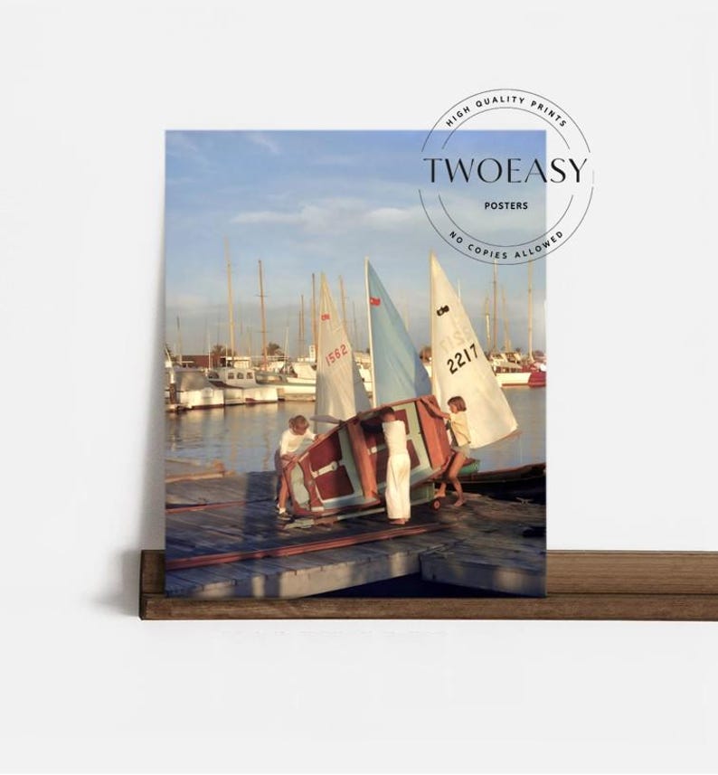 May include: A photographic print titled TWOEASY POSTERS featuring two individuals in white clothing maneuvering a small sailboat with a light blue and white sail on a wooden dock, with numerous other sailboats moored in the background water.