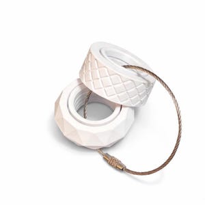 May include: Two white keyrings with geometric patterns, linked by a bronze-coloured metal cable. One has a diamond pattern, the other a faceted design. The cable has a small clasp.