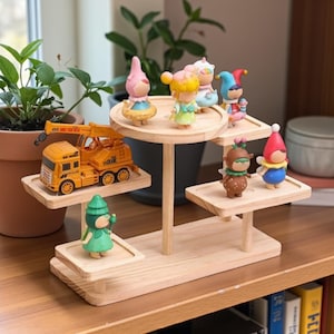 May include: A multi-tiered, light-colored wooden display stand holding various figurines and a toy crane truck. The figurines are colorful and whimsical, with gnome-like and fairy-like designs. The stand is on a wooden surface.