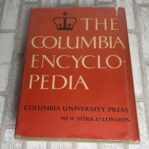 May include: A hardcover book titled The Columbia Encyclopedia with a red dust jacket. The cover features a black crown icon, gold lettering, and the text Columbia University Press New York & London printed in black at the bottom of the front cover.