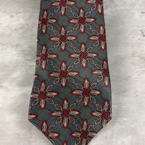 Puede incluir: Una corbata con un patrón geométrico repetitivo sobre un fondo gris oscuro. El diseño consiste en motivos entrelazados en forma de estrella delineados en rojo, con detalles en gris claro y morado que forman una estructura compleja.