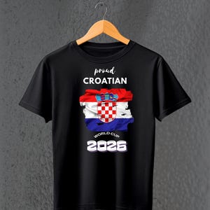 May include: Black t-shirt with the text "proud CROATIAN" above a Croatian flag design. The flag is red, white, and blue with a checkered emblem. Below the flag is "WORLD CUP 2026" in white.