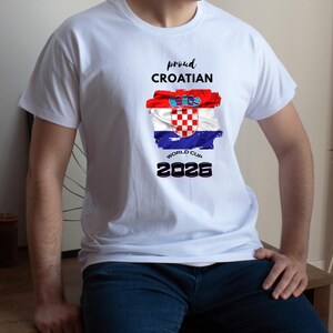 May include: White t-shirt featuring the Croatian flag design with the text "proud CROATIAN WORLD CUP 2026". The flag design includes red, white, and blue colors. The shirt is a crew neck style.
