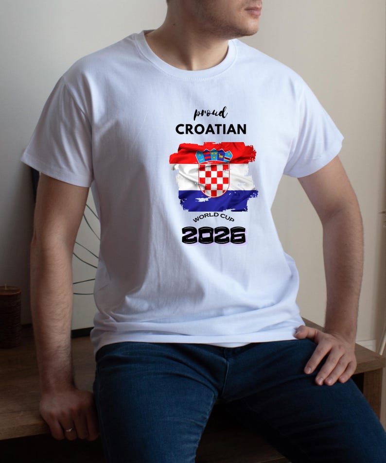 May include: White t-shirt featuring the Croatian flag design with the text "proud CROATIAN WORLD CUP 2026". The flag design includes red, white, and blue colors. The shirt is a crew neck style.
