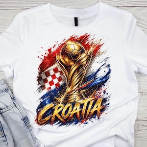 May include: White t-shirt featuring a golden soccer trophy and soccer ball design. The design includes the Croatian flag and the word "CROATIA" in gold. The design has red, white, and blue paint strokes.