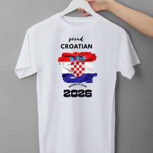 May include: White t-shirt with the text "proud CROATIAN" above a Croatian flag design. The flag is red, white, and blue with the Croatian coat of arms. Below the flag is "WORLD CUP 2026" in black.
