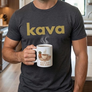 May include: A dark gray t-shirt with the word "kava" in gold lettering. A white coffee mug with a coffee cup illustration and the text "KAVA KAO KOD BAKE" is held in front of the shirt.