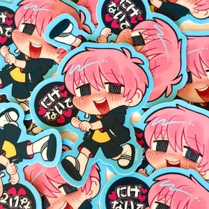 May include: A die-cut sticker featuring a cartoon character with bright pink hair, a black hoodie, and a yellow shirt. The character has swirling eyes and a wide smile. Next to the character is a circular black badge with pink hearts and Japanese text.