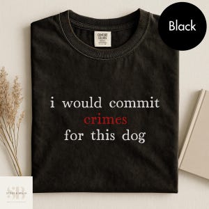 May include: Black t-shirt with the text "i would commit crimes for this dog" in white and red lettering. The shirt has a crew neck and a Comfort Colors tag. A black circle with the word "Black" is in the upper right corner.