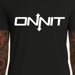 Könnte beinhalten: Schwarzes T-Shirt mit dem weißen Wort "ONNIT" und einem Pfeildesign. Das Shirt hat eine einfarbige schwarze Farbe und das Design befindet sich in der Mitte. Das Material scheint weich zu sein.