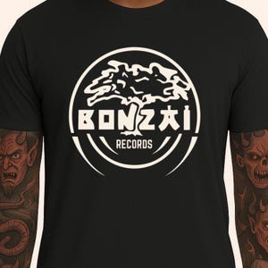 Może przedstawiać: Czarny t-shirt z białym okrągłym nadrukiem. Projekt przedstawia drzewo i napis "BONZAI RECORDS". Grafika zawiera stylizowane drzewo i zakrzywione linie. Koszulka ma okrągły dekolt.