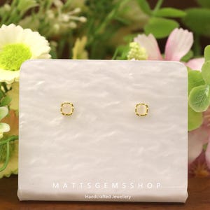 Op de afbeelding: Een paar kleine, vierkante oorstekers met een goudkleurige, getextureerde rand. De oorbellen hebben een lichtroze, vierkante middensteen. Ze worden gepresenteerd op een witte, getextureerde kaart met de tekst "MATTSGEMSSHOP Handcrafted Jewellery".