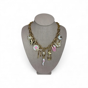 May include: Gold-tone charm necklace with various pendants, including a cat, a clock, a coffee cup, and a star. The charms are in various colors, including pink, white, and black. The necklace is displayed on a mannequin head.