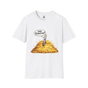 Może przedstawiać: Biała koszulka z kreskówkową igłą w stogu siana. Tekst brzmi "you found me!". Igła jest srebrna z uśmiechniętą twarzą. Stóg siana jest złoto-brązowy.