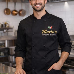 Puede incluir: Un chef sonriente con uniforme y gorra negros está en una cocina comercial. El uniforme muestra "Mario's Italian Bistro" en letras doradas, con un emblema de la bandera italiana. El chef tiene una mano en el bolsillo.