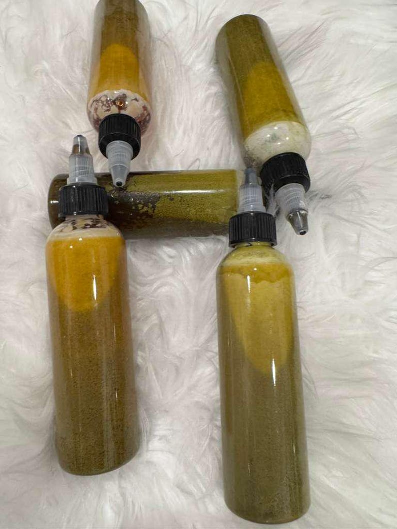 Op de afbeelding: Verschillende doorzichtige plastic flessen gevuld met een gele en groene vloeistof. De flessen hebben zwarte doppen met applicator tips. De flessen zijn gerangschikt op een witte, zachte ondergrond.