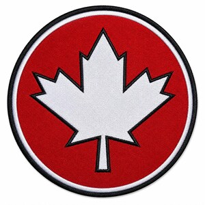 May include: Circular patch featuring a white maple leaf emblem on a red background. The leaf is outlined in black, and the patch has a black border. The design is a symbol of Canada.