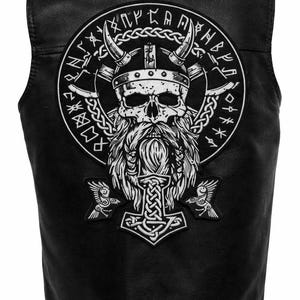 May include: Black leather vest featuring a large white graphic of a Viking skull wearing a horned helmet, with a long beard, and the symbol of Thor's hammer. The design includes runes and two ravens. The vest has a classic biker style.