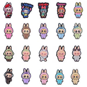 May include: A collection of colorful cartoon character charms, each featuring a bunny-like figure in various outfits. Some charms have text that reads "LABUBU" and "Powerpuff Girls". The charms are in shades of pink, blue, green, and brown.